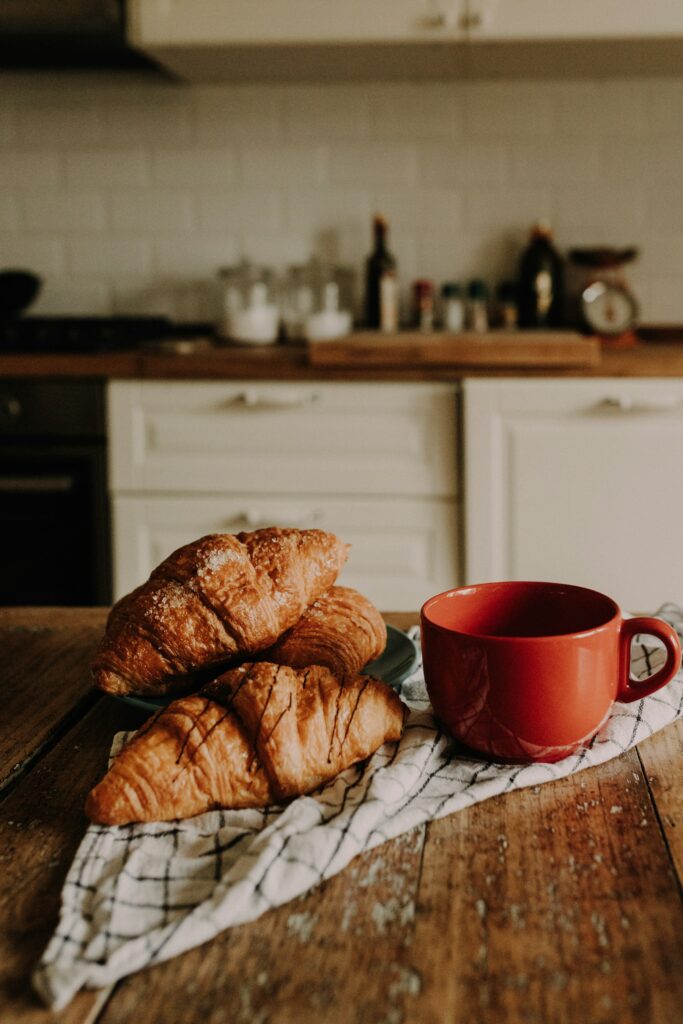 Friskbagte croissanter og en rød kop kaffe på et træbord