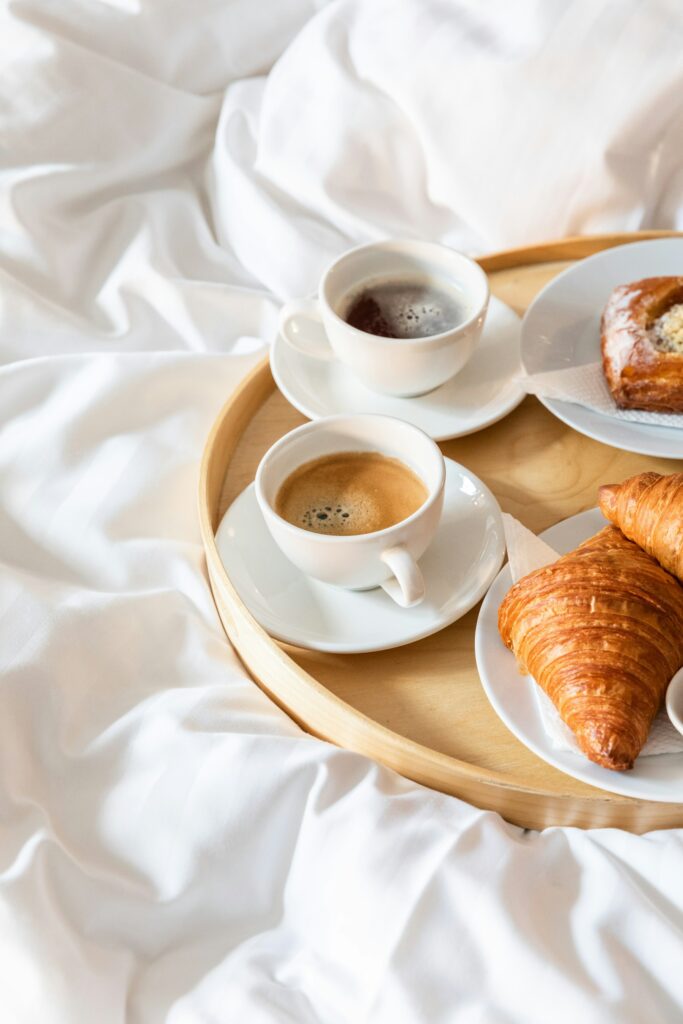 Morgenmadsbakke med kaffe og croissanter på hvidt sengelinned