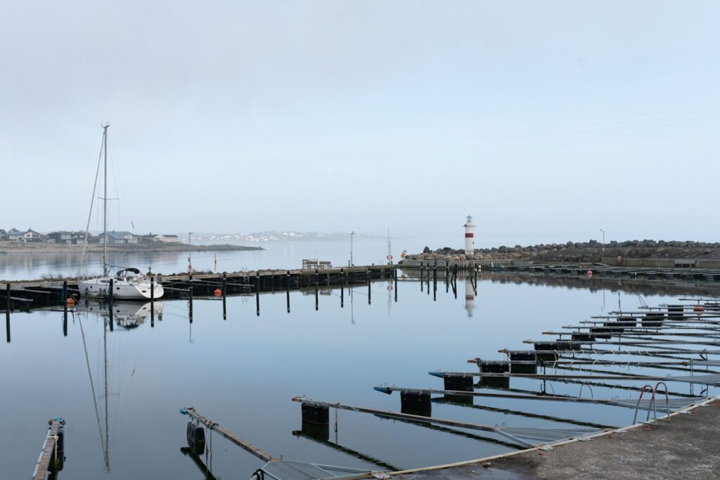 Rolig havn med sejlbåd, mole og fyrtårn i det fjerne