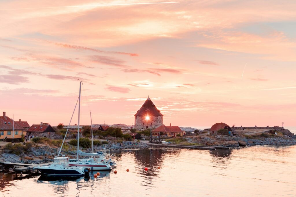 Solnedgang over en lille havn med sejlbåde og gamle huse