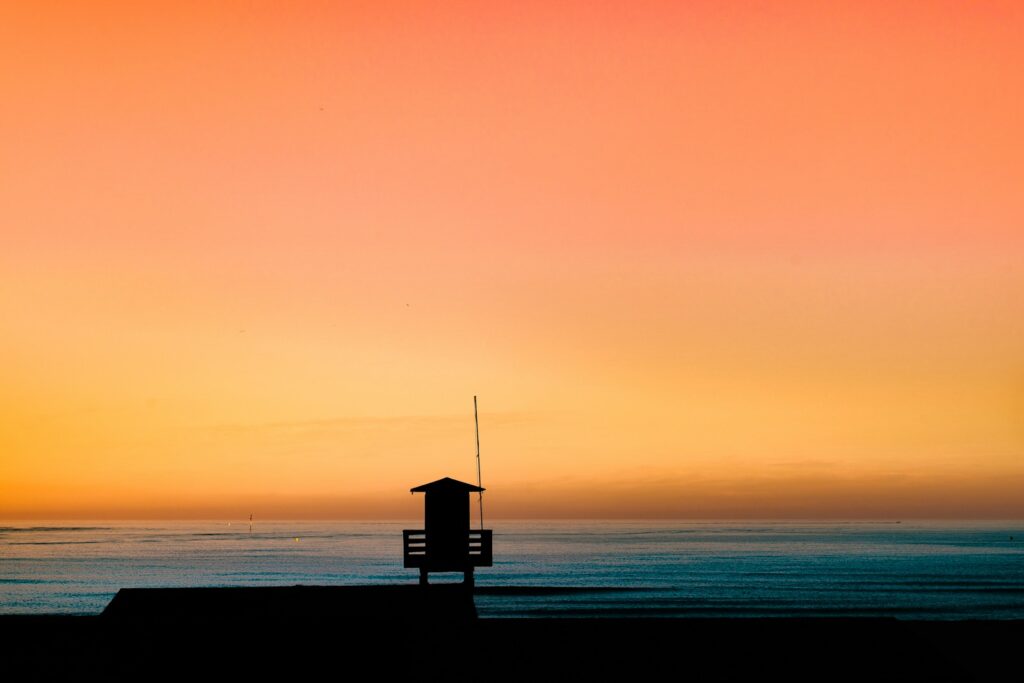 Silhuet af et lille hus ved havet i gyldent aftenlys