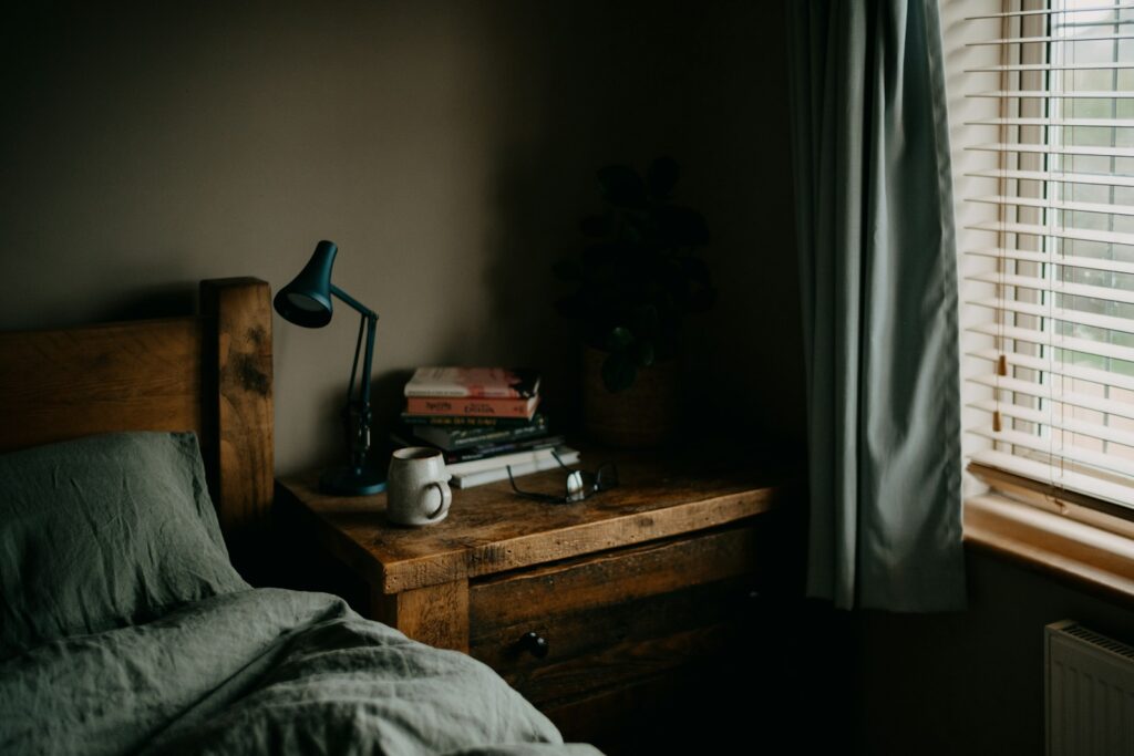 Sengebord med lampe og bøger ved et vindue