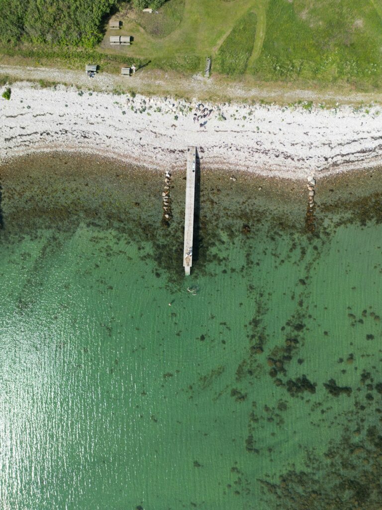 Luftfoto af en træbro ved en stenstrand og grønt vand